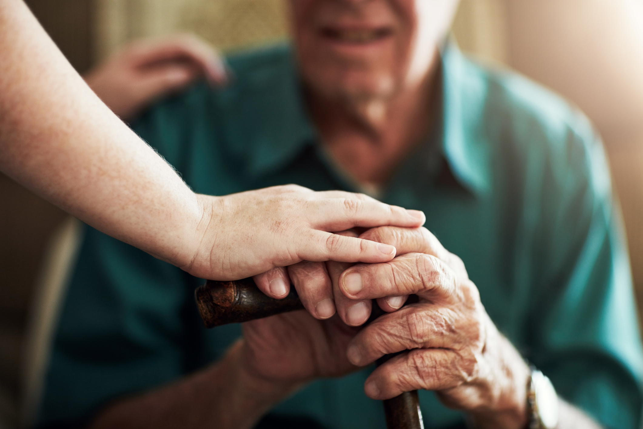 Two people holding hands over a cane.