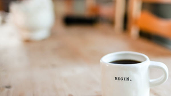White coffe mug with Begin written on it, sitting on a wodden table